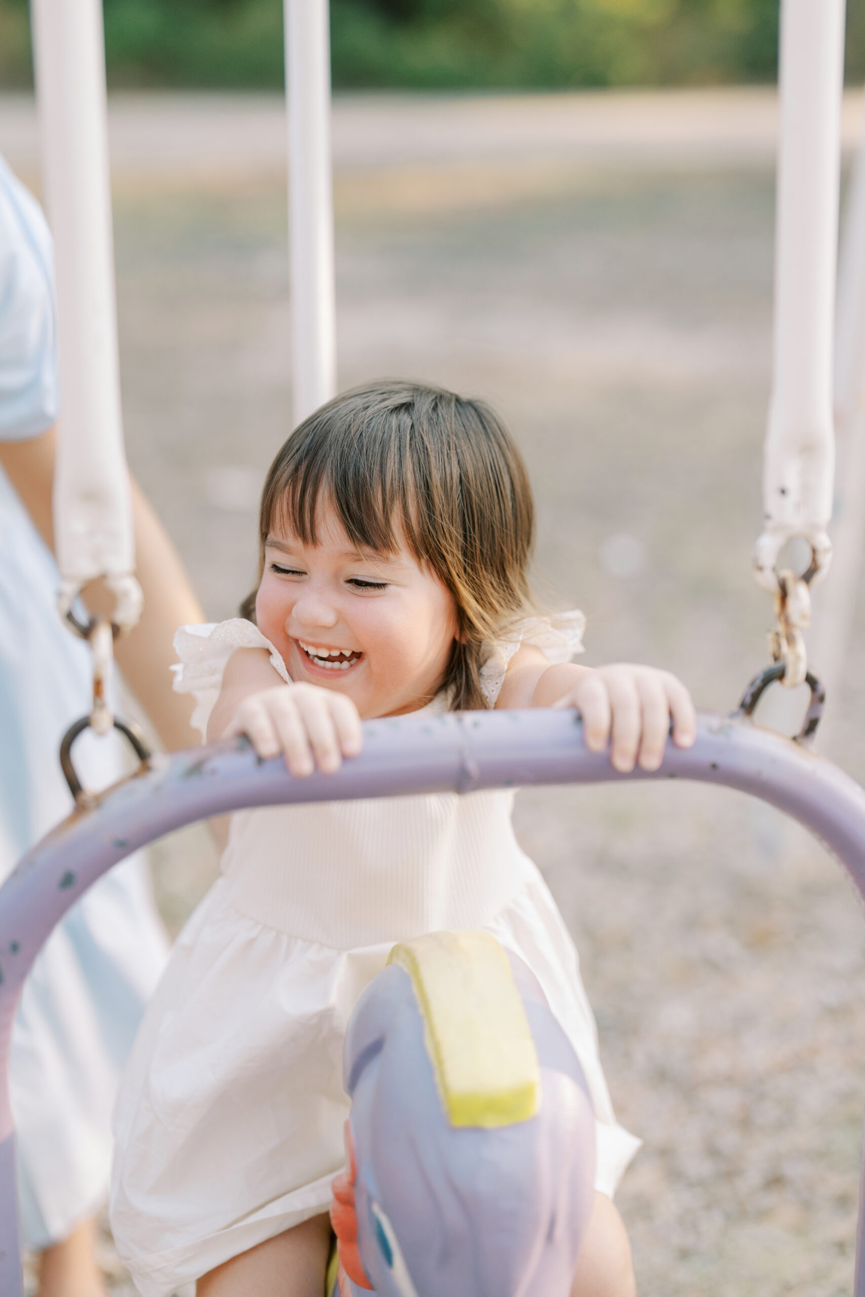 little girl smiling in sunlight while she sits on a playground swing by colorado springs photographer
