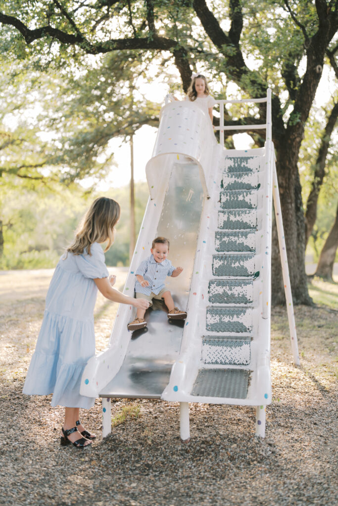 mom stands close by boy slides down slide