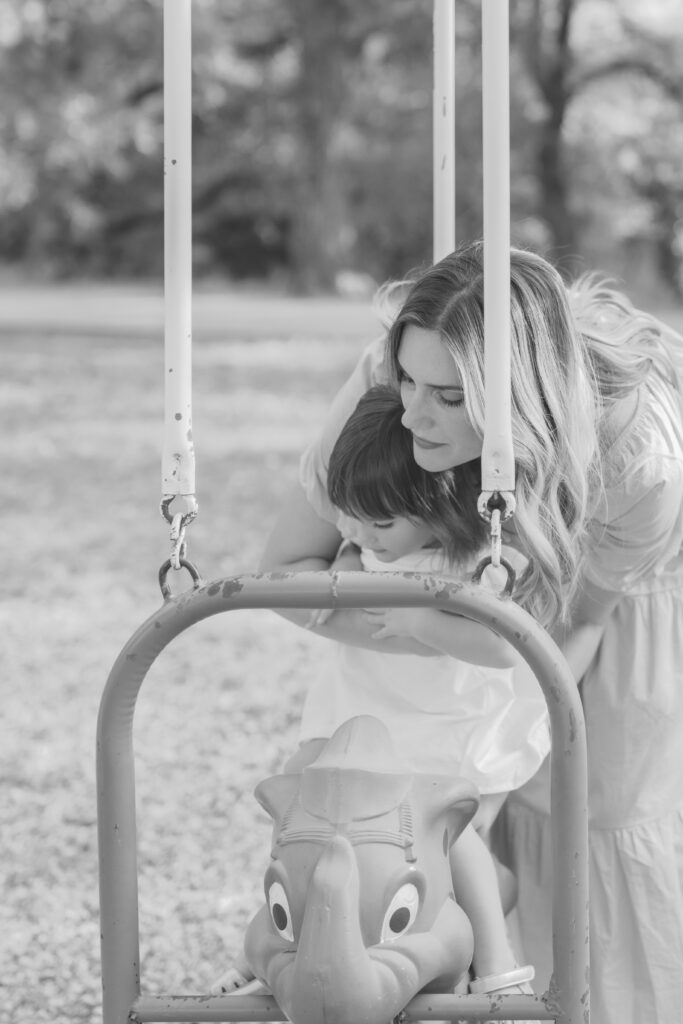 mom helping daughter onto swing at park taken by Story-Driven Family Photography in Colorado Springs