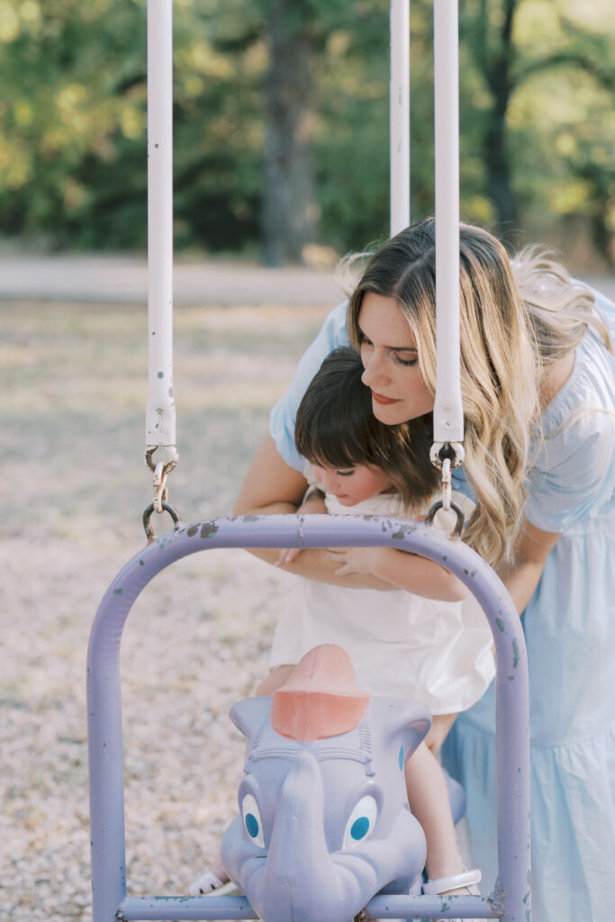 mom helping toddler on swing