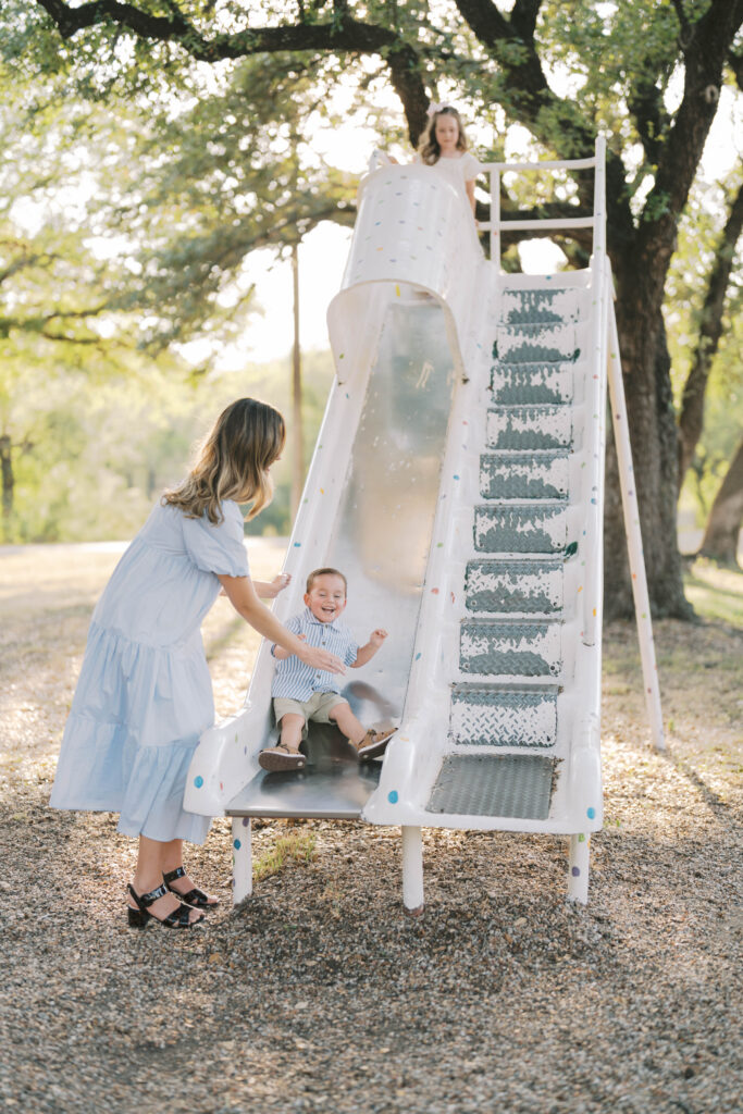 boy slides down slide while mom stands close