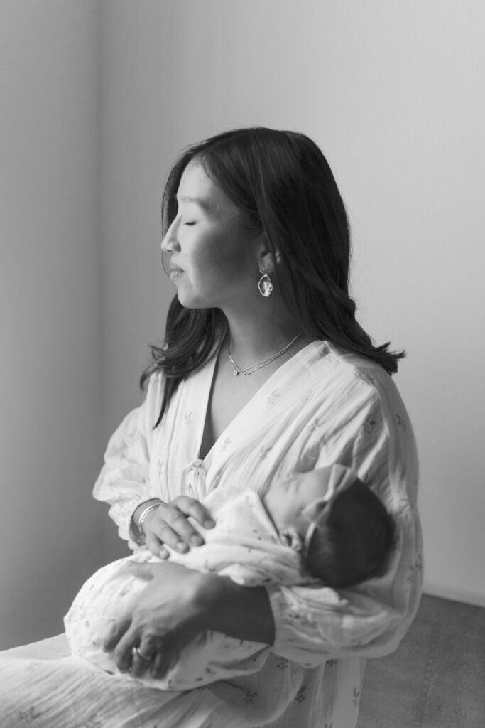 beautiful mom looking out window with new baby for newborn photographer colorado springs