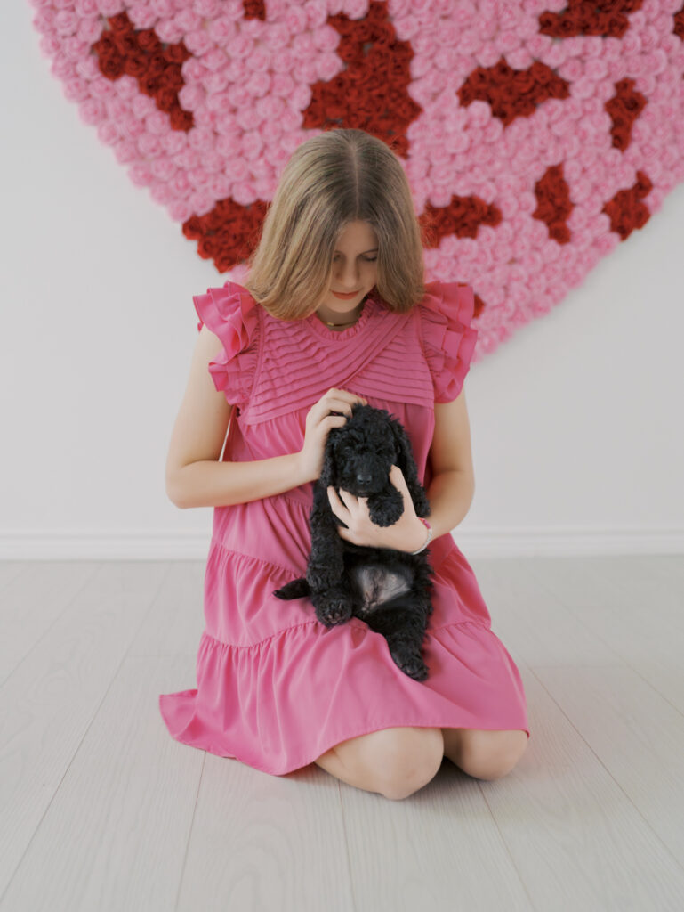 teen girl sitting on studio floor with small black doodle puppy