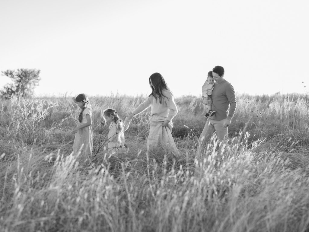 black and white image of family if five walking in a field in a line. dad holds youngest kid in arms.