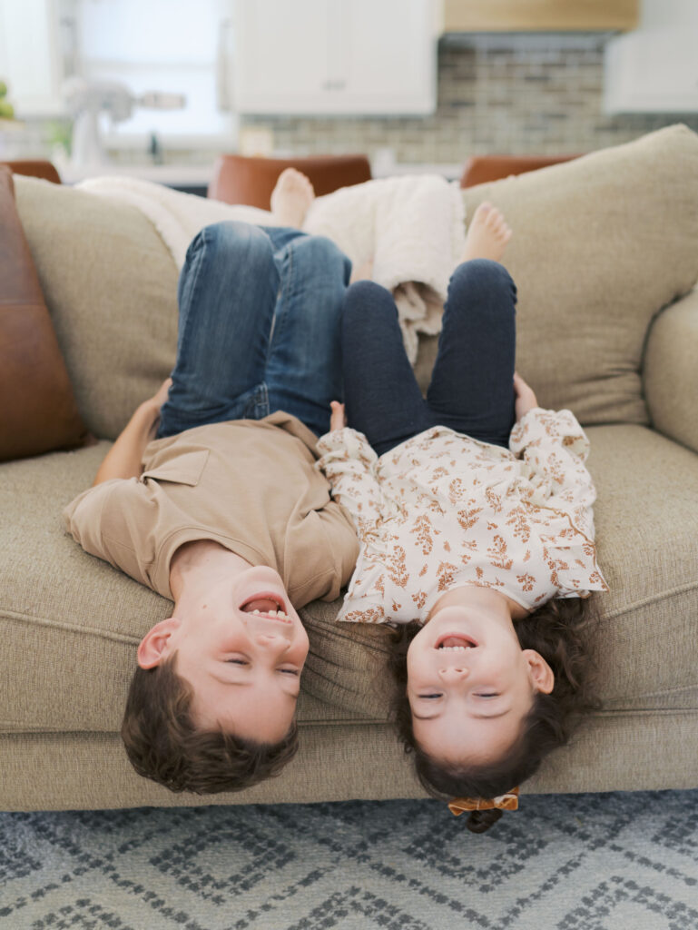 brother and sister heads upside down laughing on couch