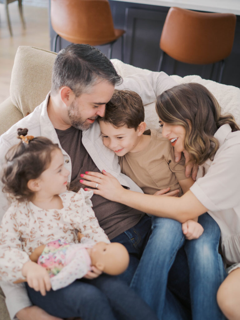 family of four lay on couch in dads arms