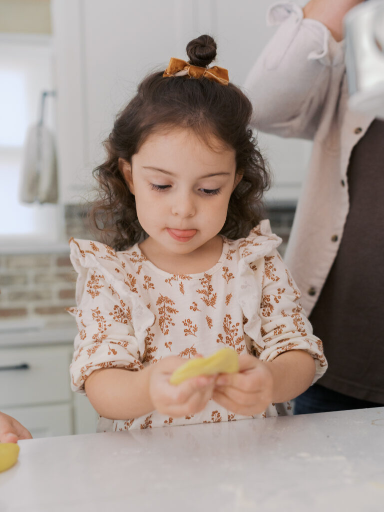 little girl with tongue out concentrating on make homemade pasta for colorado in home family session