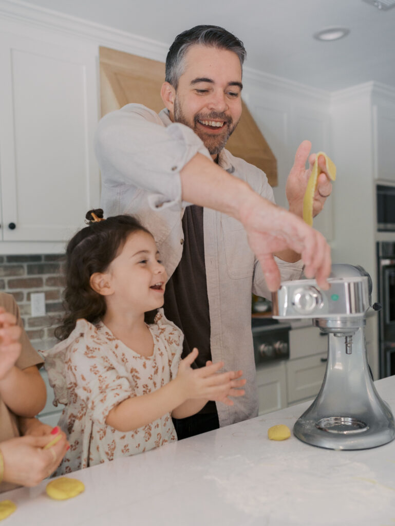 little girl smiling and clapping as dad make pasta