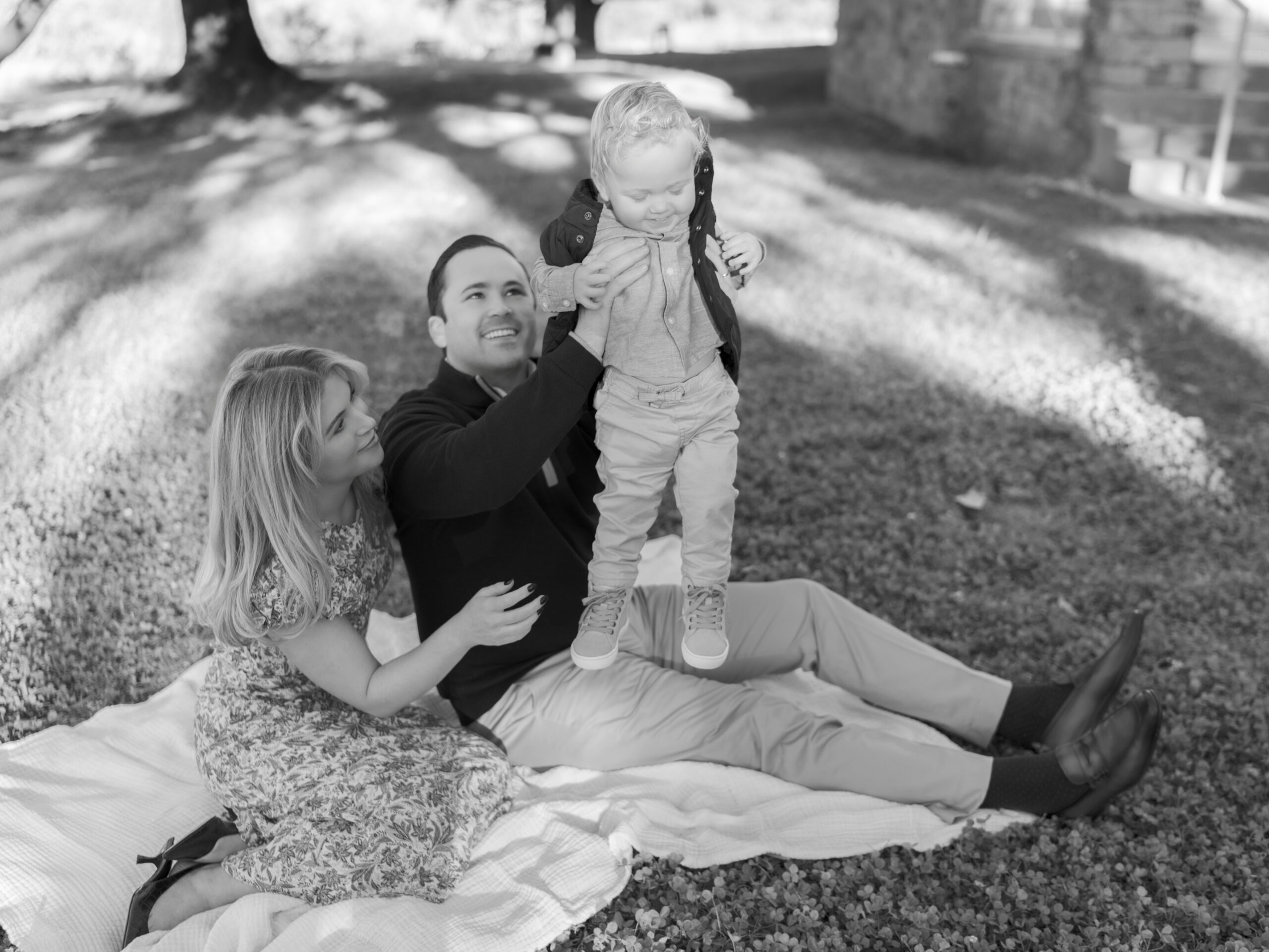 mom and dad sit on blanket and dad holds up toddler
