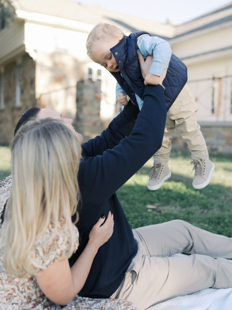 couple sitting on blanket while dad holds young son up in the air taken at a Colorado Springs Family Photos by Lauren Bounds Photography