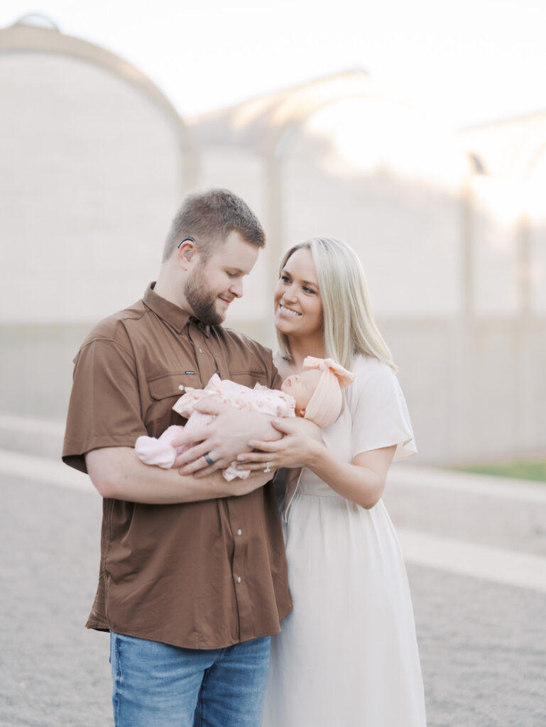 new parents embrace newborn in arms, mom is smiling at dad as he looks at newborn baby in colorado springs, co for newborn photos
