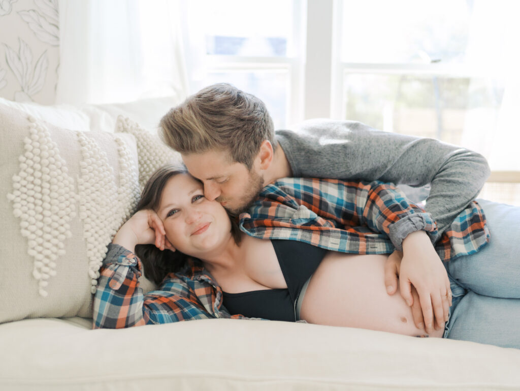 expecting mom laying on daybed with husband kissing her cheek taken by Colorado Springs Maternity Photographer Lauren Bounds