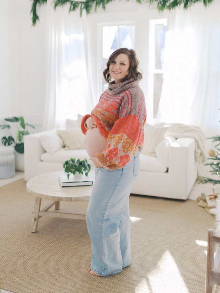 expecting in bright sweater smiling for camera with hands on belly