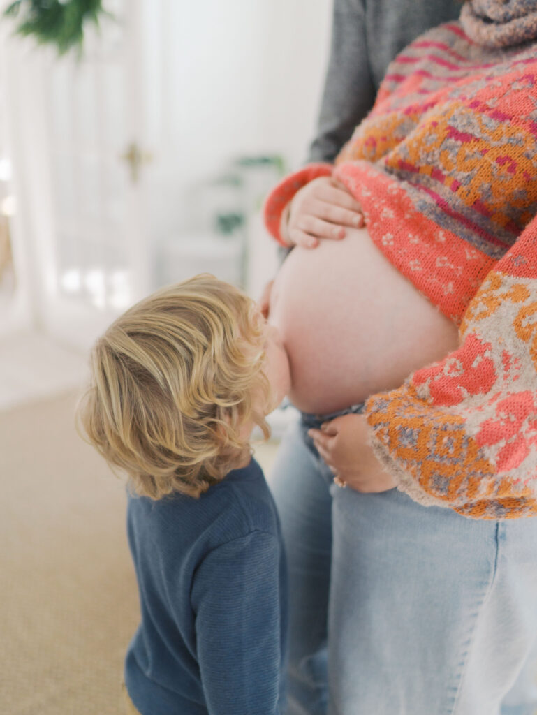 boy kissing mom's exposed expecting belly