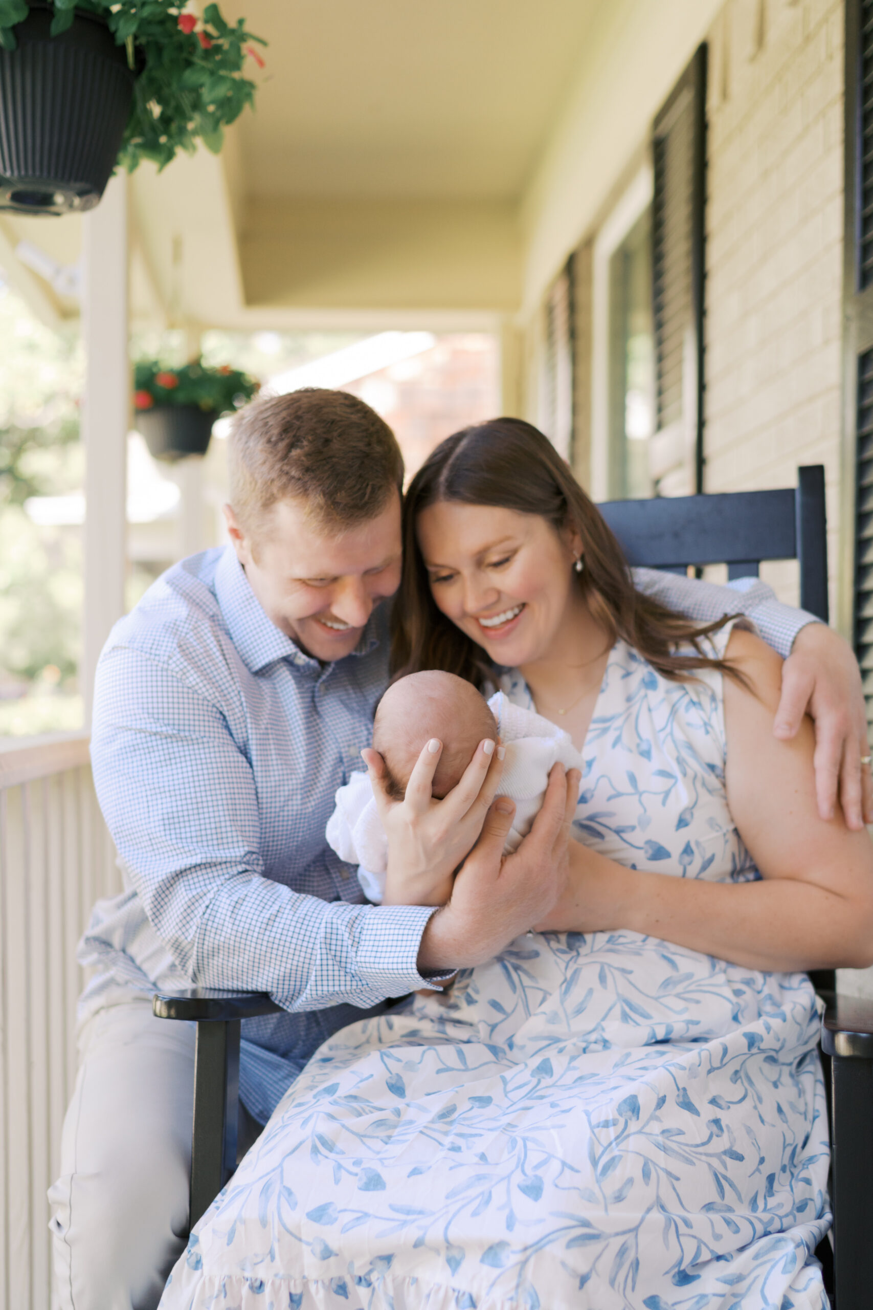 new parents on porch, mom sitting in rocking chair holding newborn baby for Colorado Springs Newborn Session