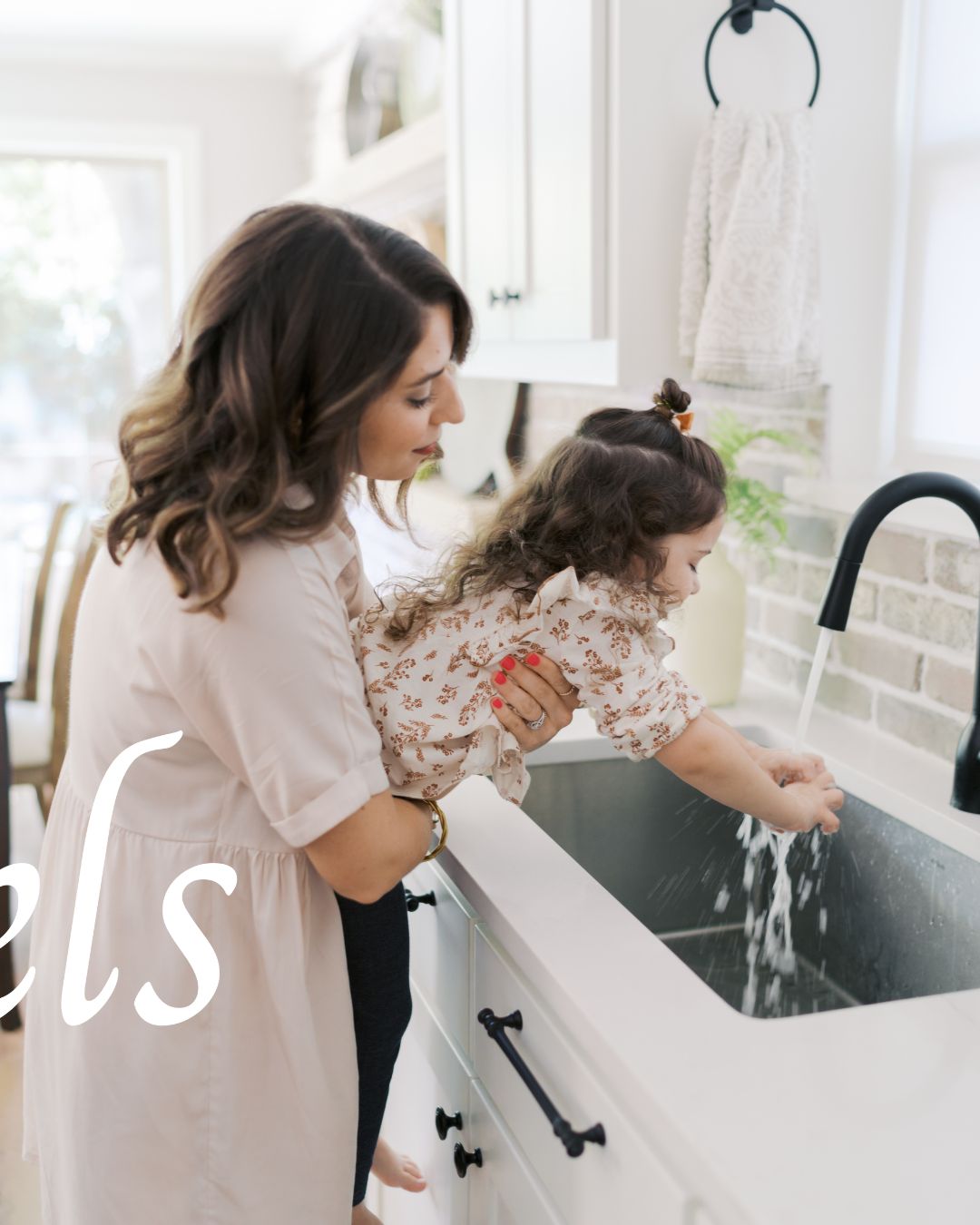 mom holding up daughter at kitchen sink to wash her hands