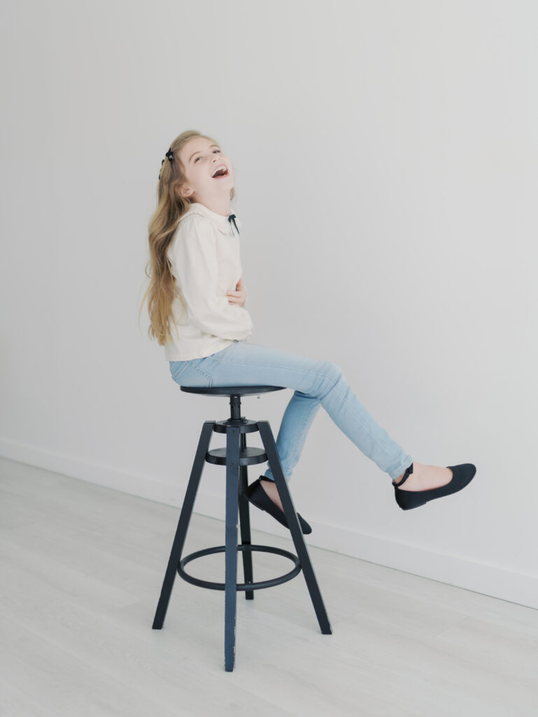 girl sitting on stool laughing with head back