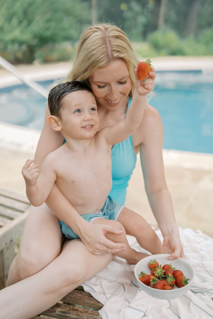 boy sitting on moms lat holding up strawberry by pool for Photography Colorado Springs