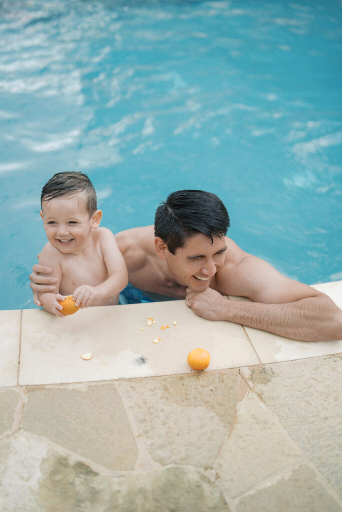 dad and boy laughing in pool eating an orange