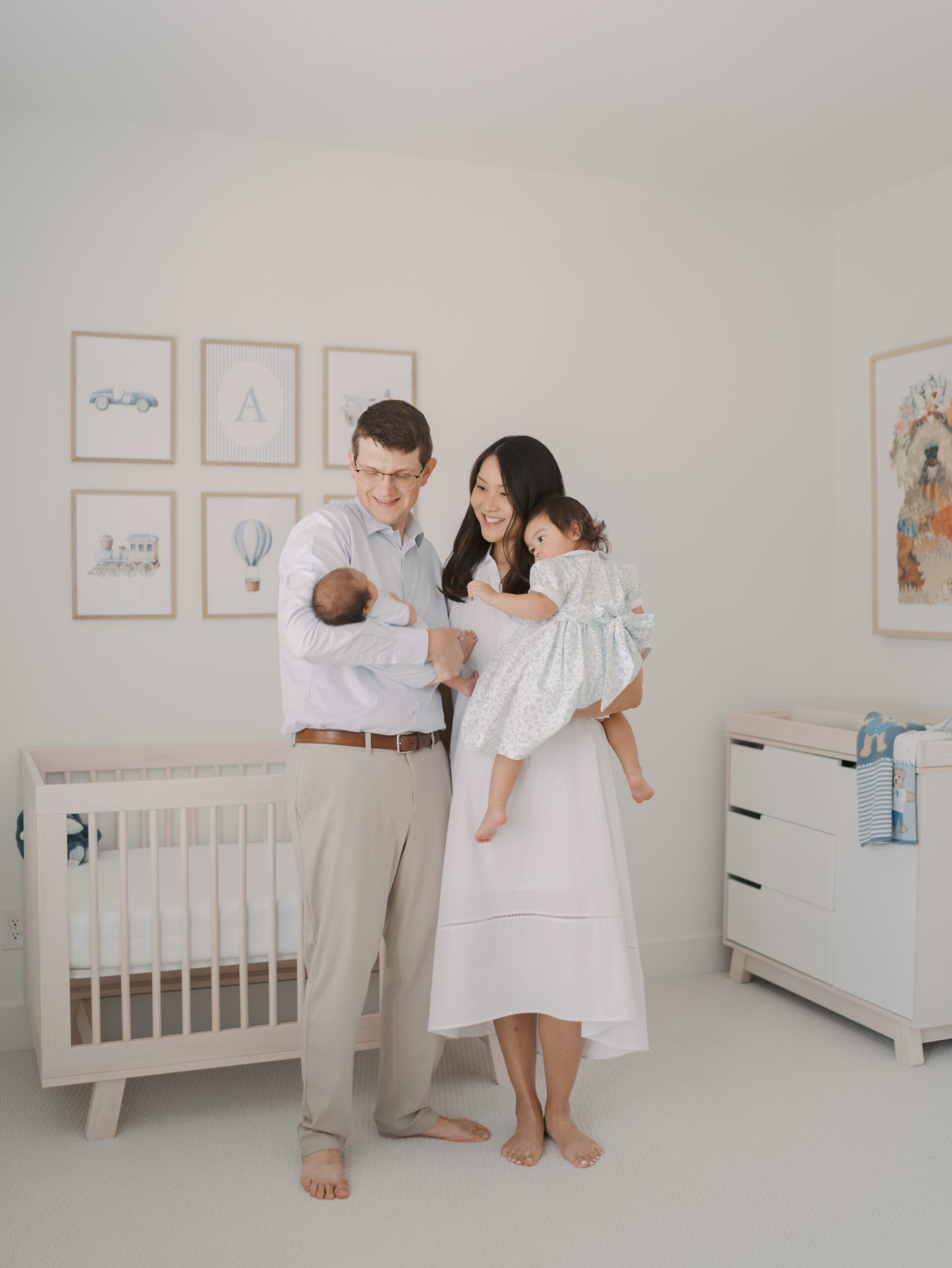 mom and dad holding newborn and toddler in baby's nursery featuring dress from colorado springs client closet