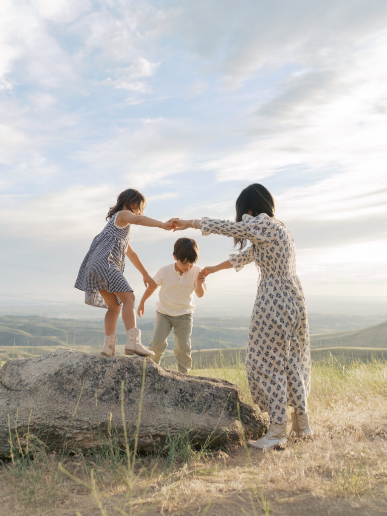 mom with kids holding hand with kids in a circle arms outstretched on rock at a Planning an adventure family session
