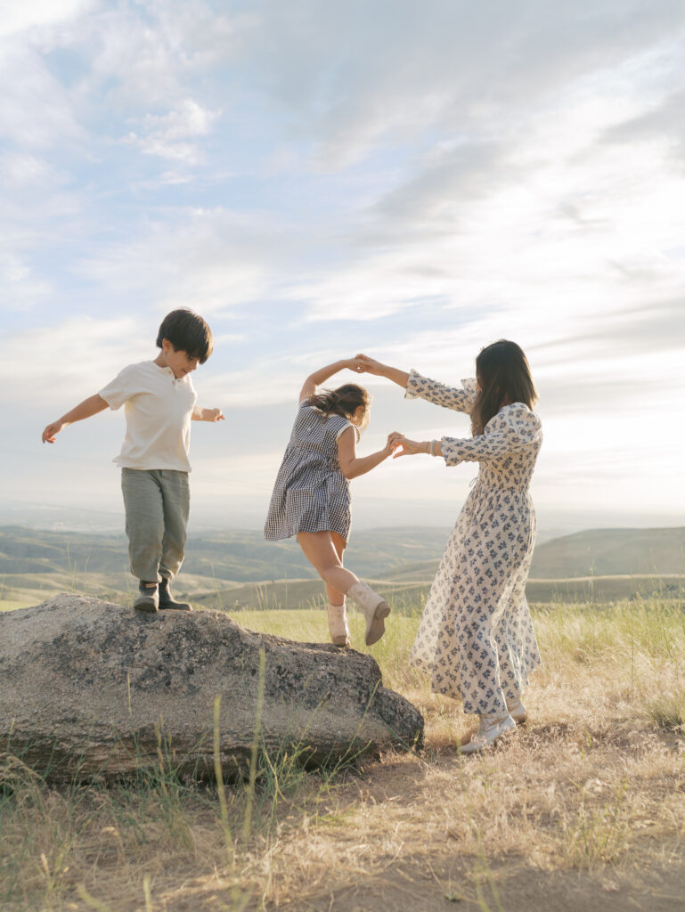 Mom and daughter dancing with little brother nearby on a rock taken by Family Adventure Photo Session photographer Lauren Bounds