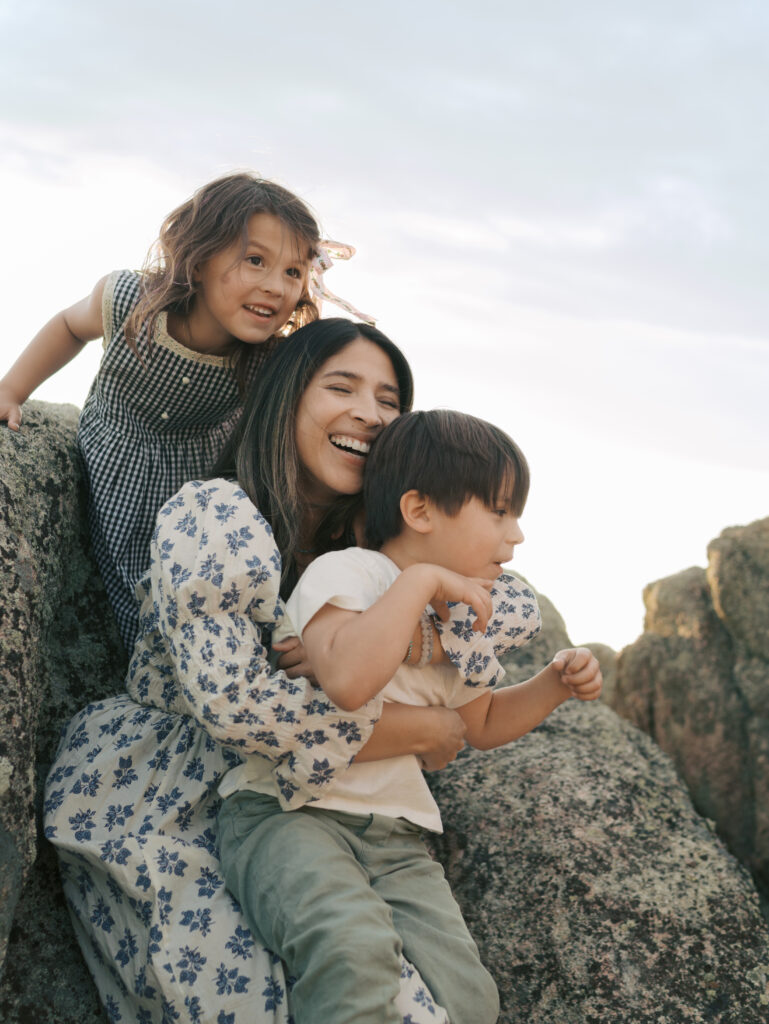 Mom hugging kids smiling big while sitting on big rocks-Family Adventure Photo Sessions by Lauren Bounds Photography