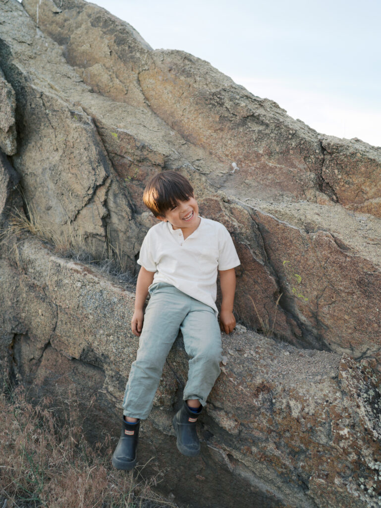 Little boy smiling while sitting on a rock. 