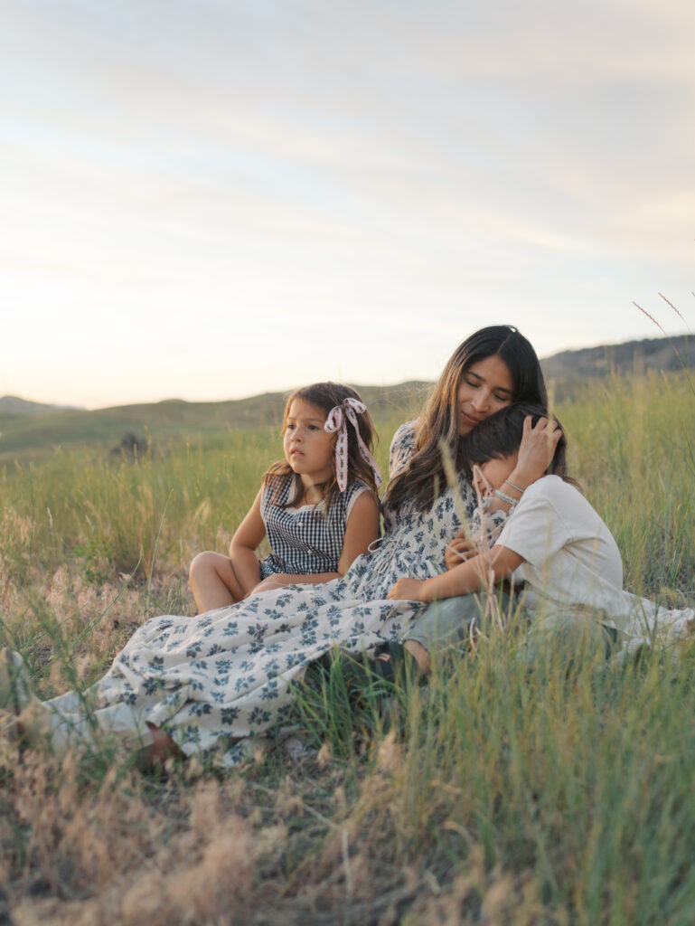 Mom hugging kids smiling big while sitting on pasture-Family Adventure Photo Sessions by Lauren Bounds Photography