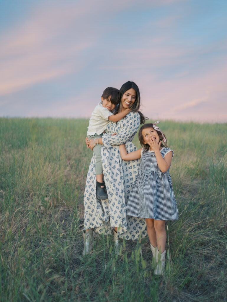 mom holding son in arm with daughter holding her arm and making noise with hand on her mouth