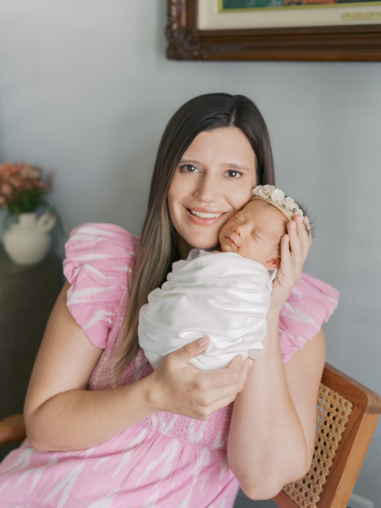 Mom smiling at camera while snuggling swaddled newborn close to face 