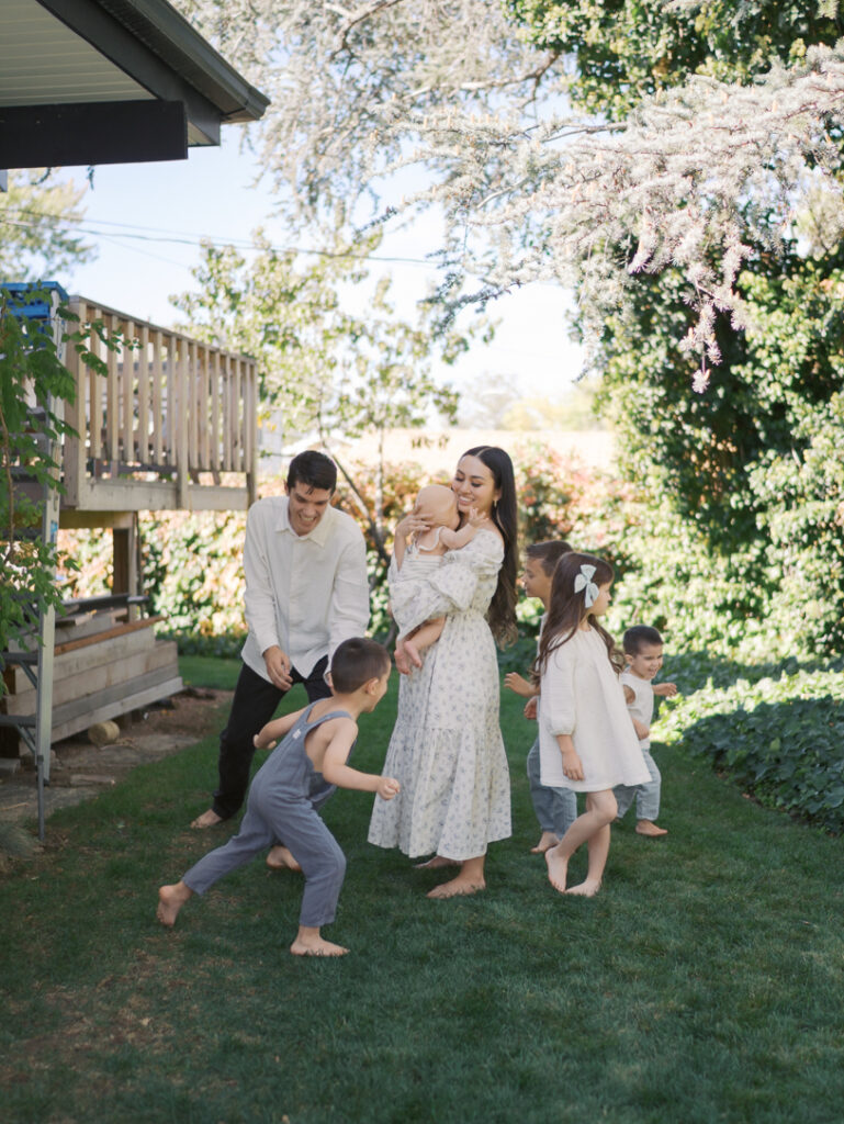 family of 7 in yard, kids running wild while mom holds baby in center