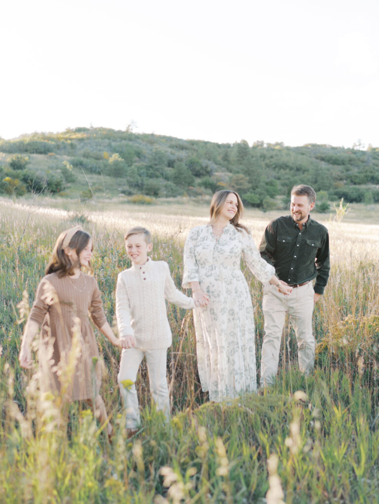 family walking in tall grass holding hands taken by Colorado Springs Maternity Photographer Lauren Bounds