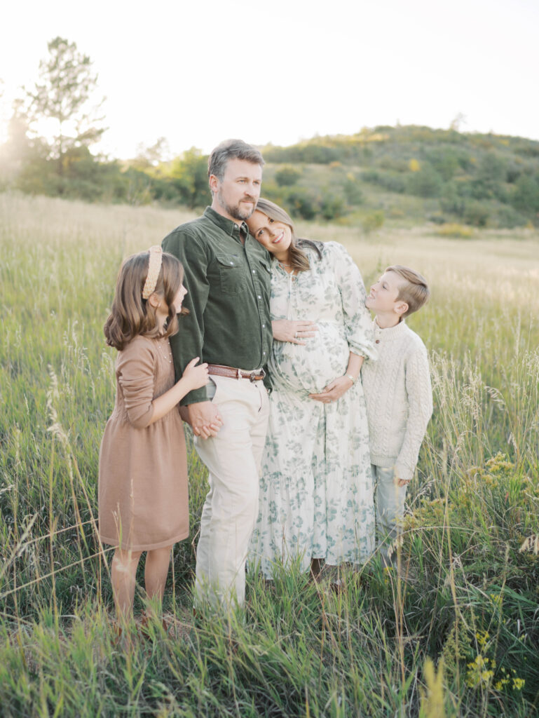 family of four standing in field embracing during Colorado Springs Maternity Photography session by Lauren Bounds