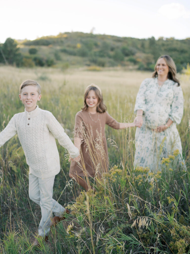 mom in field holding hands and walking with Colorado Springs Maternity Photographer Lauren Bounds