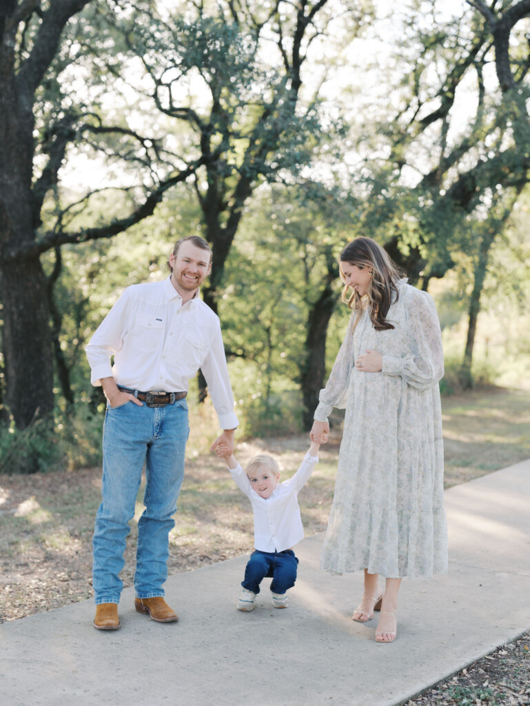 dad and mom holding hands with toddler in park