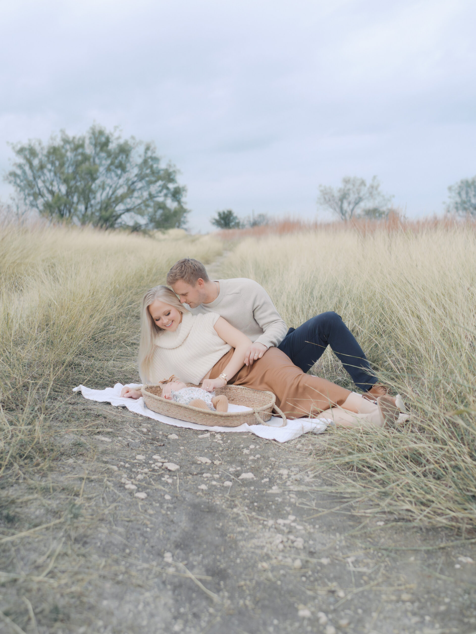 Couple laying in field with newborn baby in basket