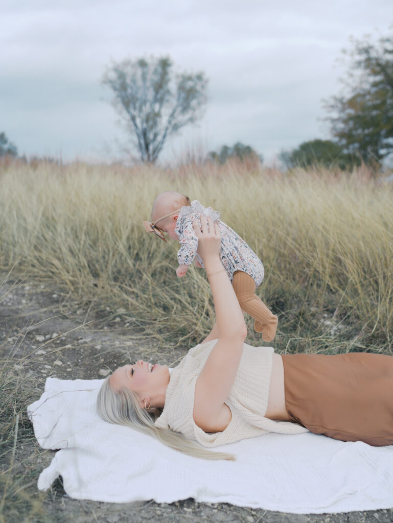 mom laying on blanket with baby extended over head smiling at a Outdoor Newborn Session in Colorado Springs