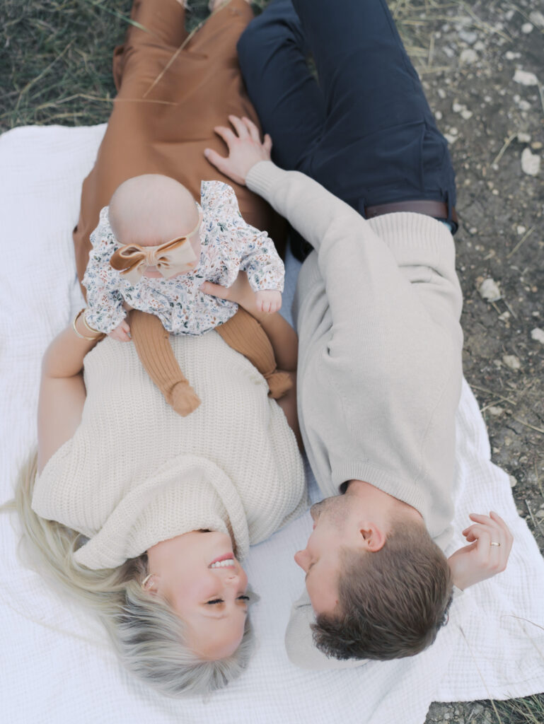 couple laying on blanket with baby sitting on mom at a Outdoor Newborn Session in Colorado Springs