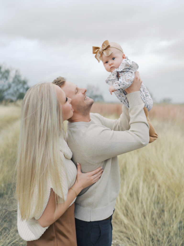 couple looks at baby in air while baby looks at camera taken at Outdoor Newborn Session in Colorado Springs