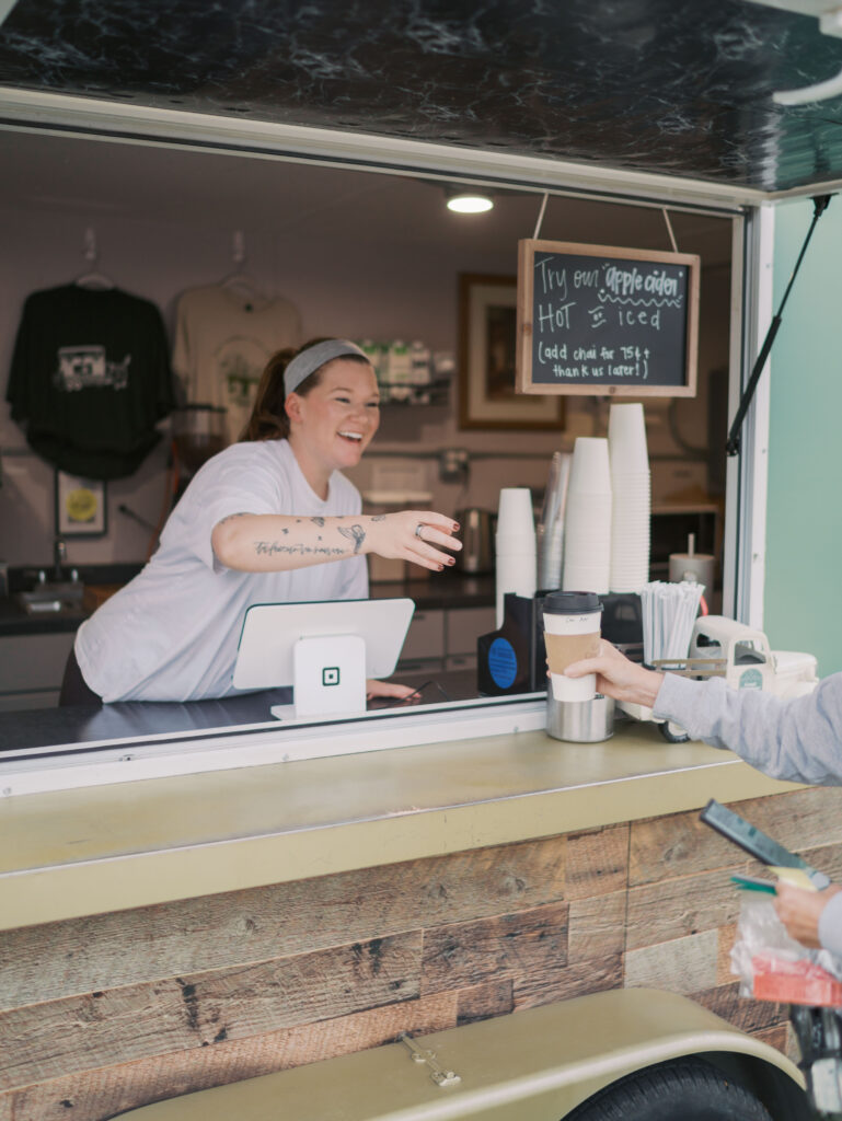 Owner of the Best Coffee Colorado Springs Good Gracious Coffee Trailer smiling while handing coffee to a customer