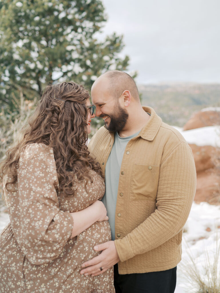 couple embracing with heads touching family gather on red rocks at garden of the gods during a maternity session in colorado springs showing what to wear for maternity photos
