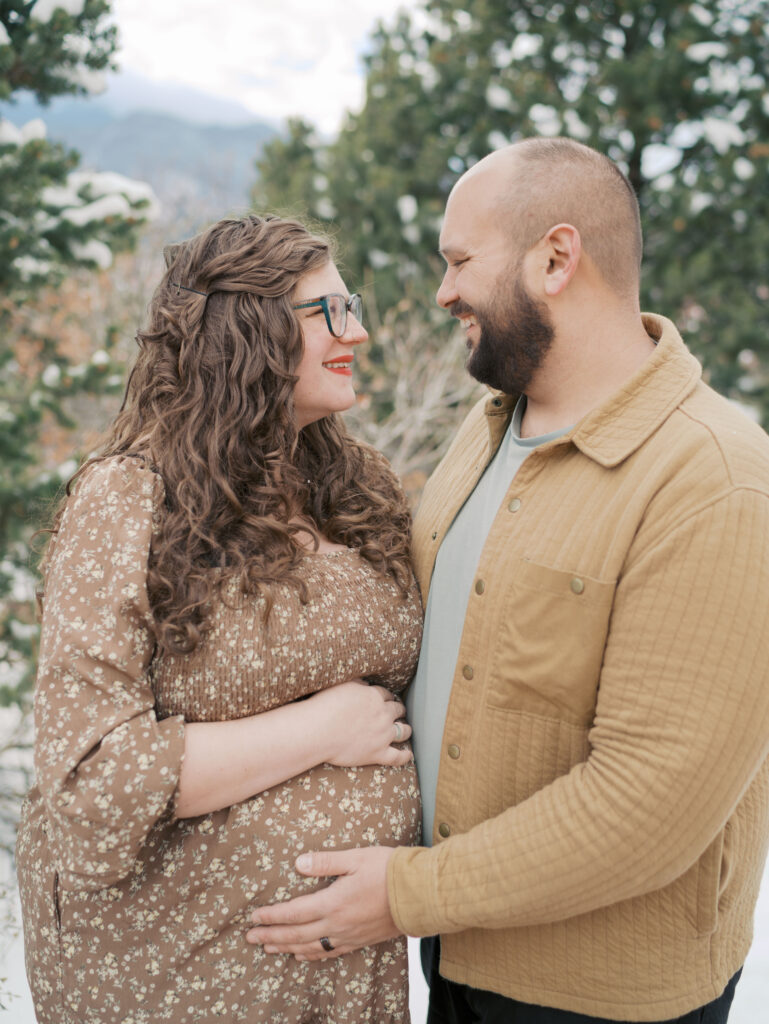 couple at Garden of the Gods Photography session looking at each other with husbands hand on wife pregnant belly