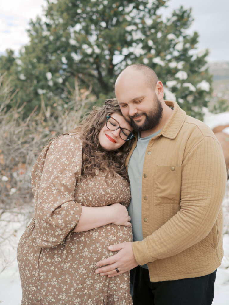 couple embracing family gather on red rocks at garden of the gods during a maternity session in colorado springs showing what to wear for maternity photos