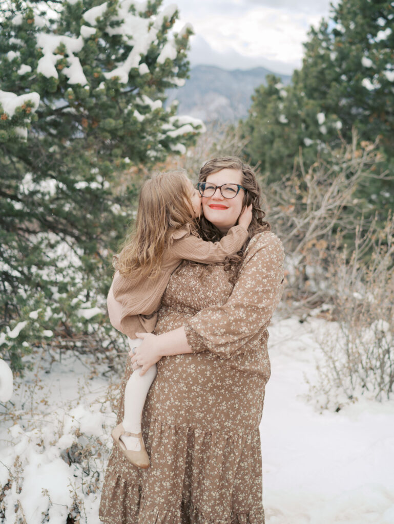 expecting mom holding young toddler as she kisses her cheek