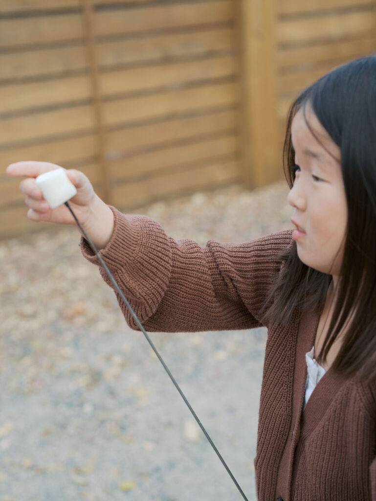 girl putting marshmallow on a stick to roast on the fire showing Winter Activities in Colorado Springs