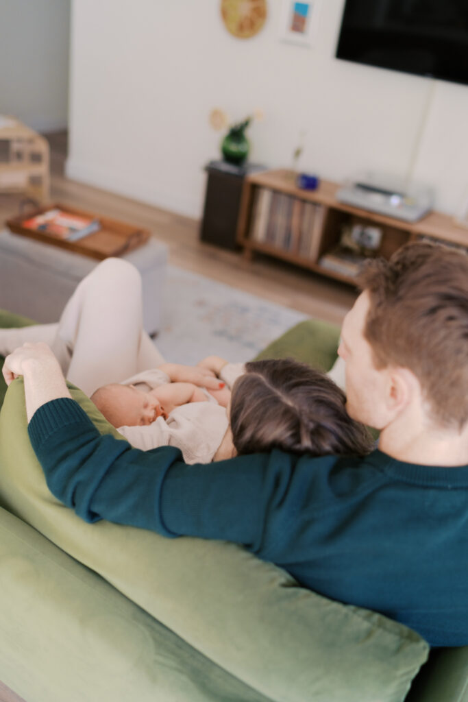 mom and dad snuggle on couch with newborn