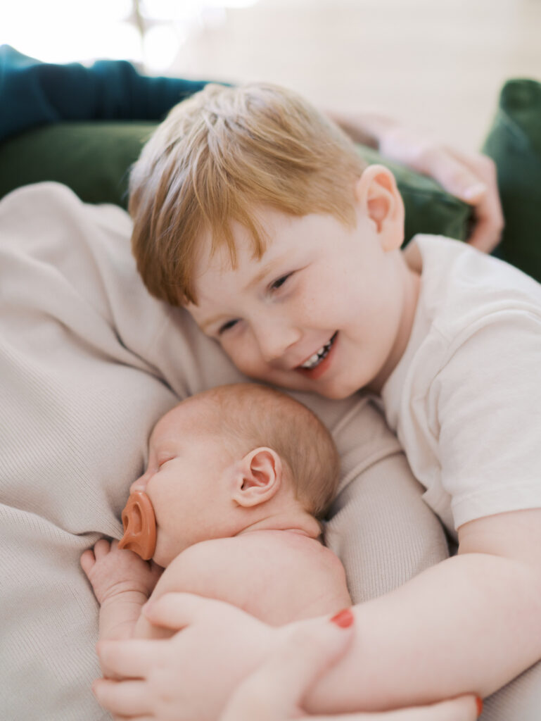big brother smiling big with hand on newborn baby