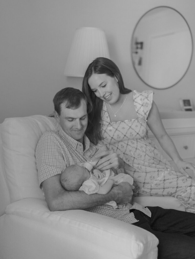 parents sitting on plush chair feeding newborn baby