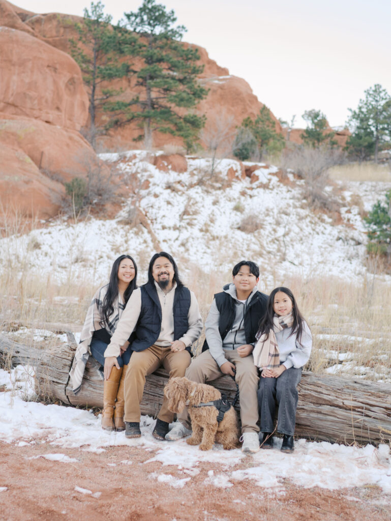family of four with small dog sitting on log for colorado springs family photos at red rock open space